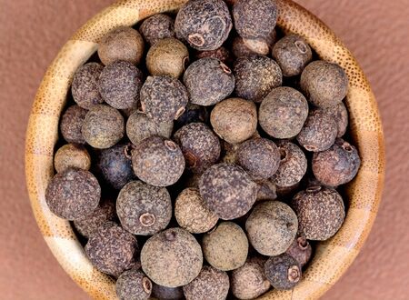 Allspice in a bamboo bowl on brown backgroundの写真素材