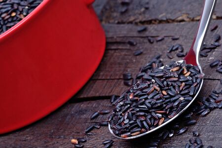 Black rice in a spoon and red pot on wooden tableの写真素材