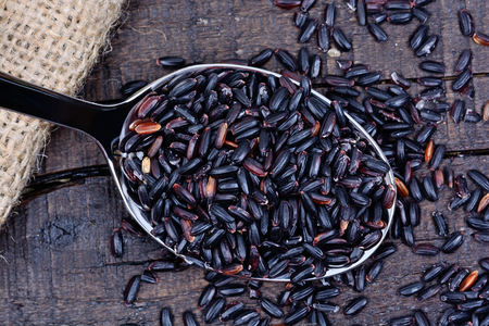 Silver spoon with black rice on wooden tableの写真素材