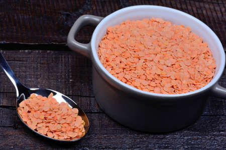Red lentils in a metal spoon and ceramic pot on table