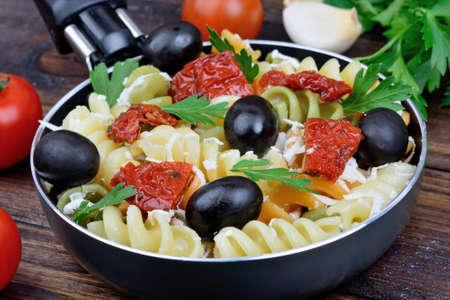 Fusilli with olive, cheese and tomato in a pan on wooden tableの写真素材