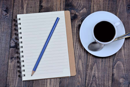 Notepad with pencil and coffee cup on wooden background closeupの写真素材