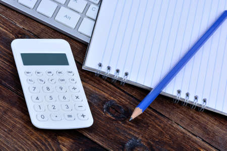 Keyboard computer with notepad and calculator on wooden tableの写真素材