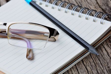 Notepad with pencil and eyeglasses on wooden table
