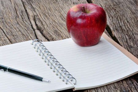 Notepad with pen and apple fruit on wooden tableの写真素材