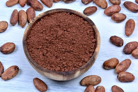 Cacao powder in a bowl with beans on white wooden tableの写真素材