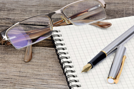 Notebook with fountain pen and eyeglasses on wooden tableの写真素材