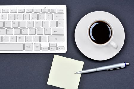 Office desk table with empty notes, coffee cup and keyboard computer on black backgroundの写真素材