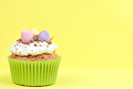 Easter cupcake with chocolate eggs on yellow background