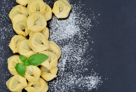 Italian traditional tortellini pasta and white flour on slateの写真素材