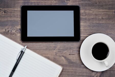 Empty digital tablet pc with notebook and coffee on a wood tableの写真素材