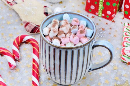 Hot chocolate in a mug with colorful marshmallow and christmas ornament on shiny tableの写真素材