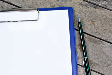 Close up of clipboard with blank white paper and pen on rustic tableの写真素材