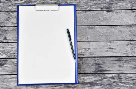 Clipboard with blank white paper with pen on an old wooden table