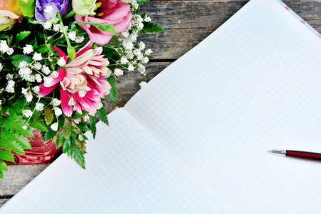 Empty notebook with pen, flowers and clock on an old wood tableの写真素材