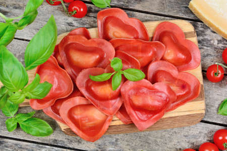 Close up of plate with red heart ravioli with cherry tomato, mozzarella, parmesan and basil on tableの写真素材