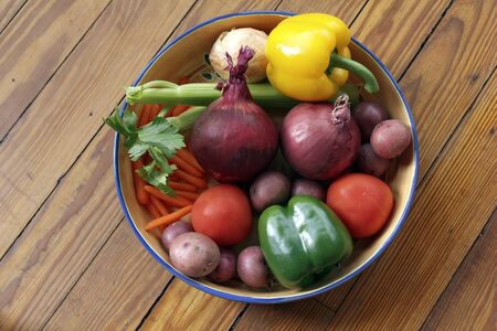 Assorted vegetables on a wooden table with peppers, onions, potatoes, carrots, celery, tomatoesの写真素材