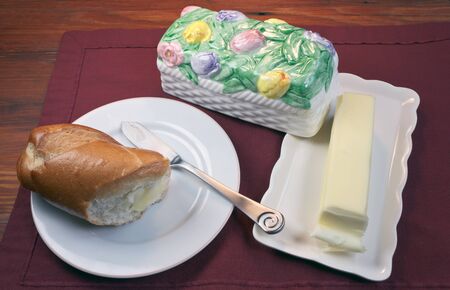 Bread on a plate with butter knife and Butter on a butter dish with floral coverの写真素材