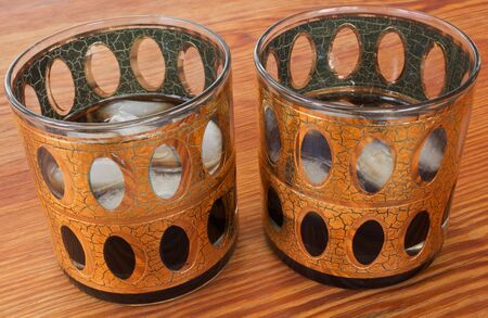 Old-fashion, 1974 glasses with ice and whiskey on a wood table. Gold Trimmed.の写真素材