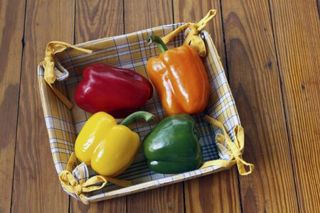 Assorted Bell Peppers in red, green, orange, yellow in a cloth basket on a wooden tableの写真素材