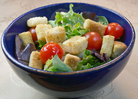 Salad in a blue bowl and on a textile with assorted greens, croutons, tomatoes.の写真素材