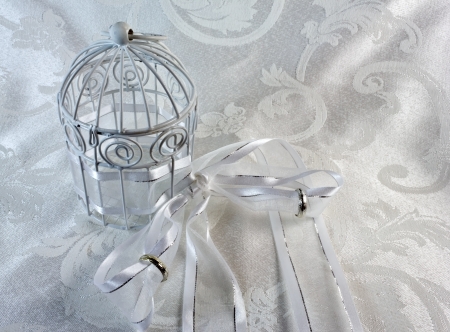 White Cage, Ribbon, and Wedding Bands on a brocade textile. The cage is closed with rings on the ribbonの写真素材