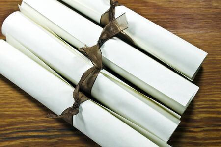 Diplormas or Certificates rolled and tied with ribbon on a wooden surface