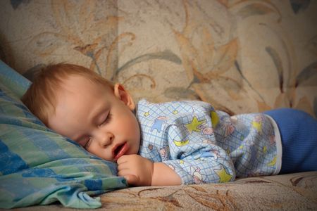 The sleeping small, beautiful boy laying on a sofa with an open mouth