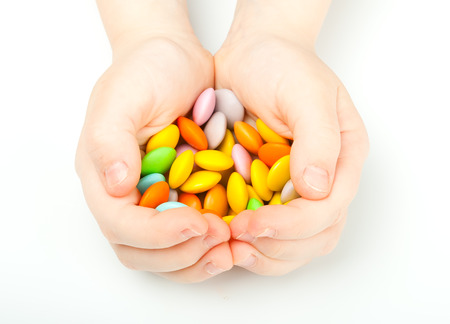 Childrens hands holding colorful candy on white backgroundの写真素材