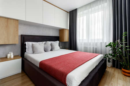 Bedroom in an apartment with a bed tucked into a red bedspread and gray pillowsの写真素材