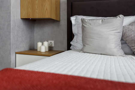 Bedroom in an apartment with a bed tucked into a red bedspread and gray pillows