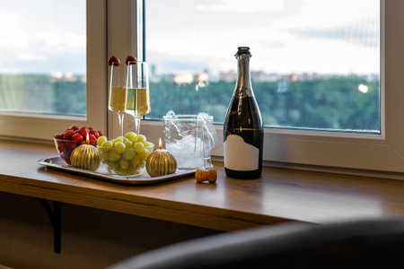 Champagne glasses with strawberries and grapes next to the candles against the background of the window.の写真素材