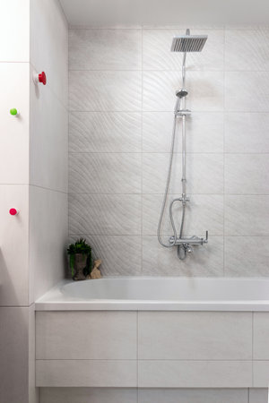 Classic style bathroom with bathtub and shower behind glass wall and simple wall and floor tiles.
