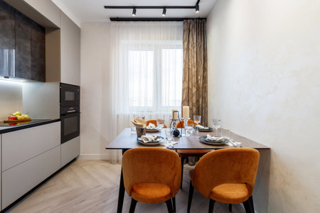 Modern kitchen combined with the dining room in dark and light colors, with orange chairs and glass cabinets for dishes.の写真素材