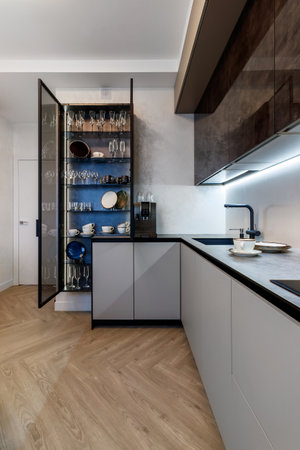 Modern kitchen combined with the dining room in dark and light colors, with orange chairs and glass cabinets for dishes.の写真素材