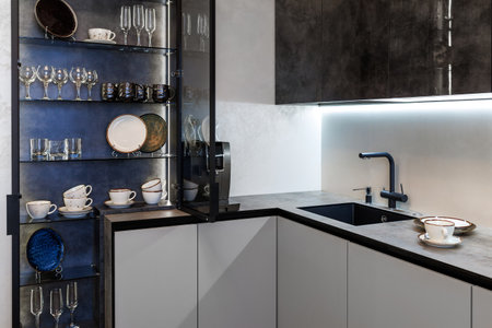 Modern kitchen combined with the dining room in dark and light colors, with orange chairs and glass cabinets for dishes.の写真素材