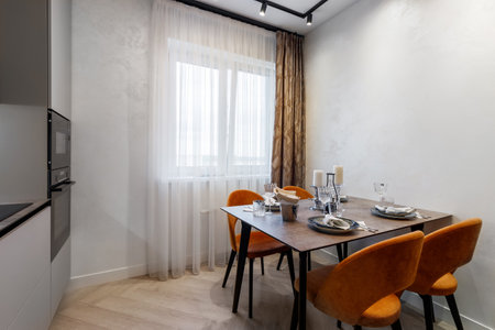 Modern kitchen combined with the dining room in dark and light colors, with orange chairs and glass cabinets for dishes.の写真素材