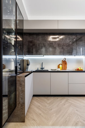 Modern kitchen combined with the dining room in dark and light colors, with orange chairs and glass cabinets for dishes.の写真素材