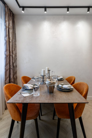 Modern kitchen combined with the dining room in dark and light colors, with orange chairs and glass cabinets for dishes.の写真素材