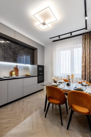 Modern kitchen combined with the dining room in dark and light colors, with orange chairs and glass cabinets for dishes.の写真素材