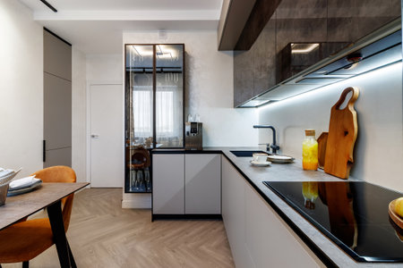 Modern kitchen combined with the dining room in dark and light colors, with orange chairs and glass cabinets for dishes.の写真素材