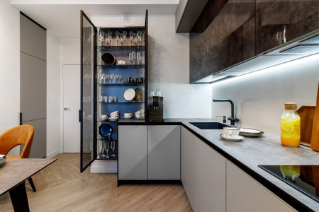 Modern kitchen combined with the dining room in dark and light colors, with orange chairs and glass cabinets for dishes.の写真素材