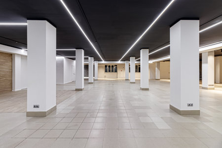 A large empty room with ceramic tiles on the floor, a black ceiling with lighting and columns...