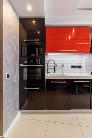 Modern kitchen interior with red and black cabinets and white ceramic floor.の写真素材