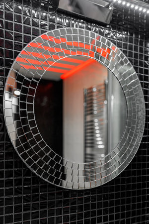 A round mirror on a black wall is made of small square tiles in the mosaic style.の写真素材