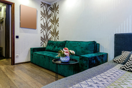 Bed and green sofa in a modern room with a bouquet of flowers on a black coffee tableの写真素材