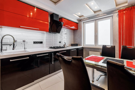 Modern kitchen interior with red and black cabinets and white ceramic floor.の写真素材