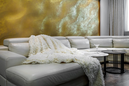 Living room with white walls and a huge white sofa, a black glossy wardrobe with a large yellow 3D panel on the wallの写真素材