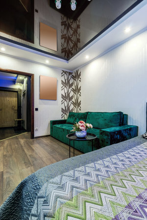 Bed and green sofa in a modern room with a bouquet of flowers on a black coffee tableの写真素材