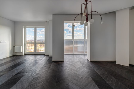 Empty apartment with large floor-to-floor window overlooking nature and blue sky with clouds.の写真素材